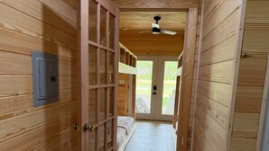 Un corridoio in legno con una porta che dà su una stanza con un letto e una ventola a soffitto.