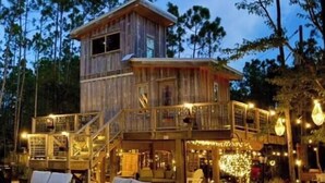 A two-story wooden cabin with a balcony, outdoor seating, and string lights.