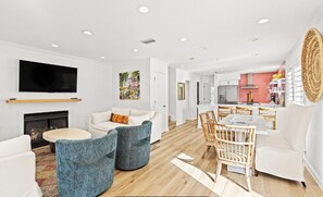 A modern living room with a fireplace, a flat-screen TV, and a dining area with wicker chairs. - 🦩Book Me Baby! Bahama Mama in Miramar Beach🦩 (Miramar Beach)