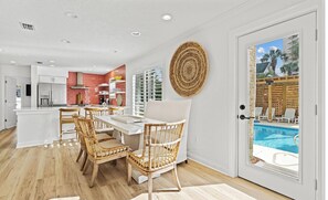 A modern kitchen with white cabinets, a dining area with wicker chairs, and a view of a swimming pool through a glass door. - 🦩Book Me Baby! Bahama Mama in Miramar Beach🦩 (Miramar Beach)