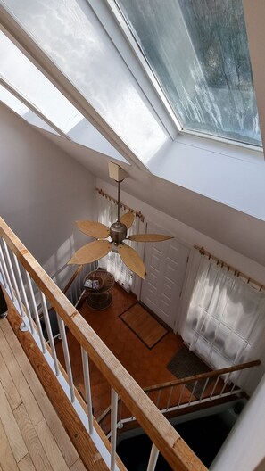 Ein Zimmer mit Oberlichter, Deckenventilator, einer Holztreppe und einer Tür.