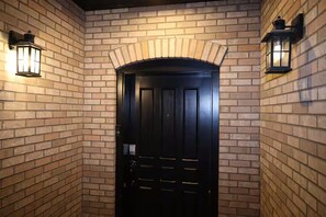 Una puerta negra con un arco de ladrillo y dos faroles fijados a la pared.