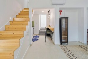A staircase leading to a dining area with a patterned rug, a cabinet, and a sign indicating an emergency exit. - Green Near The Sea, By Home Match (Setúbal)
