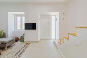 Una sala de estar moderna con un sofá, un televisor de pantalla plana montado en la pared, un tapete estampado y una escalera con escalones de madera.