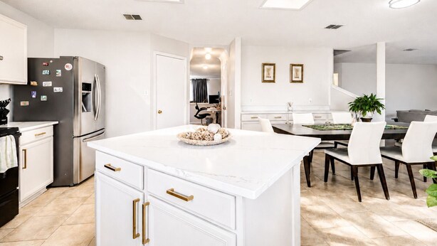 Una cocina moderna con armarios blancos, una isla central y un comedor con mesa y sillas.