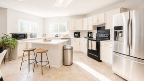 Una cocina moderna con armarios blancos, una isla central, taburetes de bar, un refrigerador de acero inoxidable y una estufa negra.
