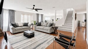Amplia sala de estar con un conjunto de sofás, una mesa de centro, un televisor y una escalera.