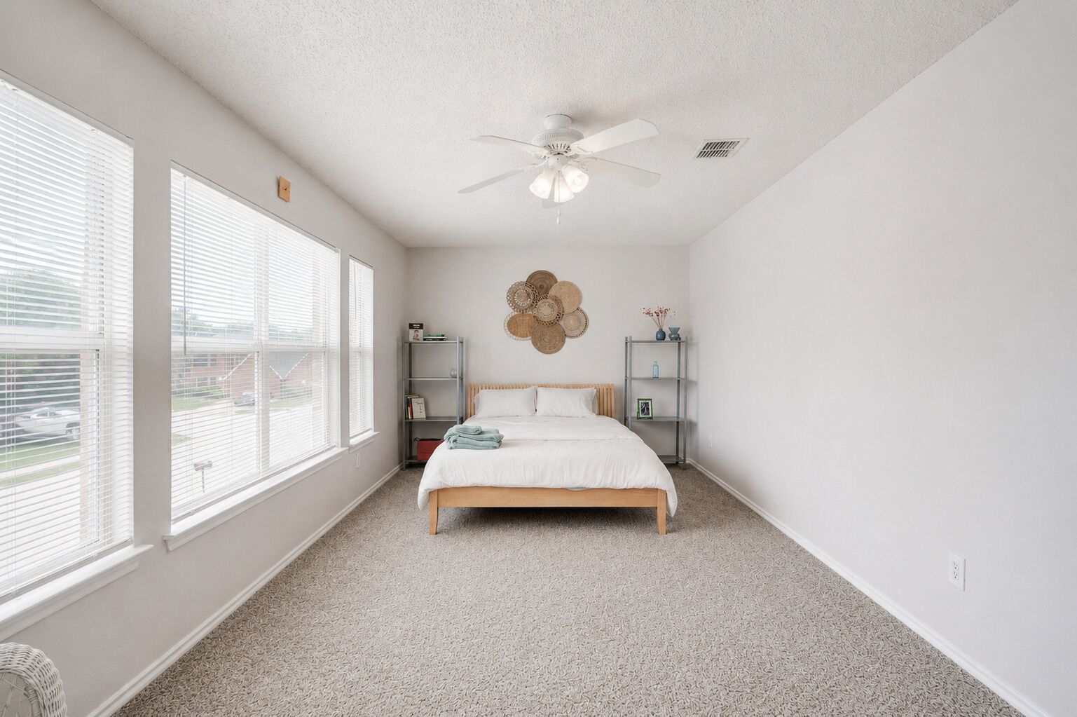 A bedroom with a bed, a ceiling fan, a window, and a wall-mounted shelf.