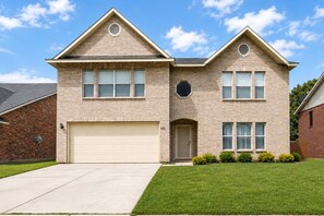 A two-story house with a garage, a front door, and a small porch with potted plants.