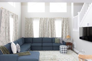 Ein Wohnzimmer mit einem Ecksofa, einem Fernseher, einer Lampe und einem gemusterten Teppich.