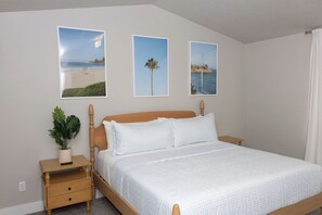 Ein Schlafzimmer mit einem Bett, einem Nachttisch mit Pflanze und drei gerahmten Bildern an der Wand.