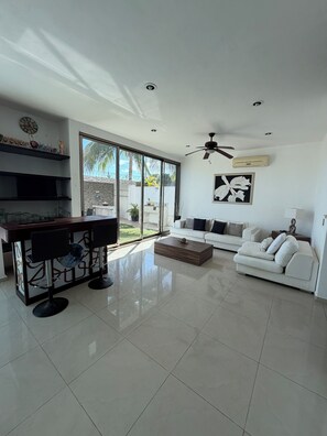 A spacious living area with a white sofa, a coffee table, a bar area with stools, and a ceiling fan. - Luxury house with pool (Cancún)