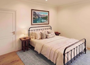 A bedroom with a bed, a nightstand, a lamp, a framed picture on the wall, and a door.