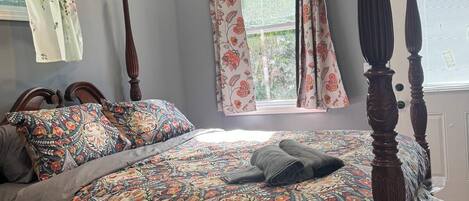 Una cama con dosel con una colcha estampada, una ventana con cortinas y un ventilador de techo.