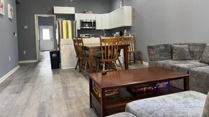 Ein modernes Wohnzimmer mit einem Holzespeisetisch, einem grauen Sofa und einer Küche im Hintergrund.