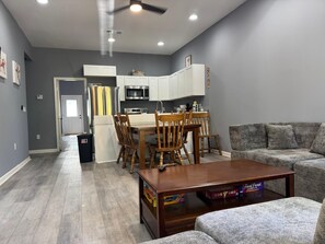 Ein modernes Wohnzimmer mit einem Holzespeisetisch, einem grauen Sofa und einer Küche im Hintergrund.