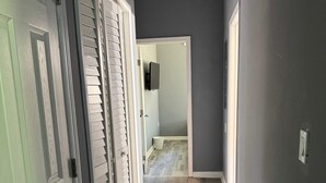 Ein Flur mit einer zur Toilette führenden Tür, einem Lüftungsgitter in der Decke und einem Lichtschalter an der Wand.
