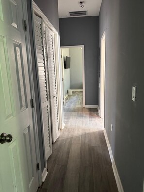 Ein Flur mit einer zur Toilette führenden Tür, einem Lüftungsgitter in der Decke und einem Lichtschalter an der Wand.