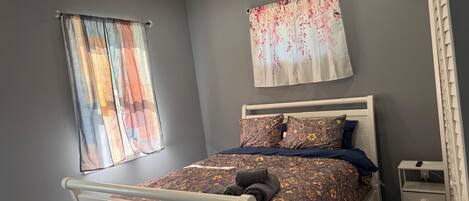 A bedroom with a bed, two curtains, a ceiling fan, and a nightstand.