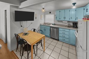 Une cuisine compacte avec des meubles bleus, une table à manger en bois et un lave-vaisselle encastré.