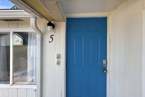 Une porte bleue portant le numéro 5, une fenêtre blanche et un cadre de porte blanc.