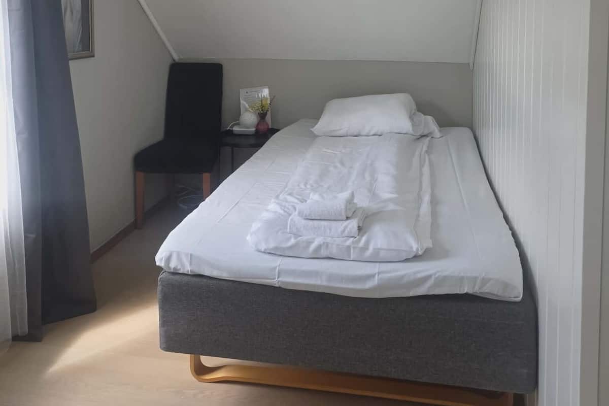 A small, modern bedroom with a single bed, a chair, and a desk.
