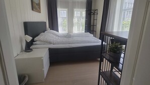 A bedroom with a bed, bedside table, lamp, and a window with curtains. - Stavangerliving (Stavanger)