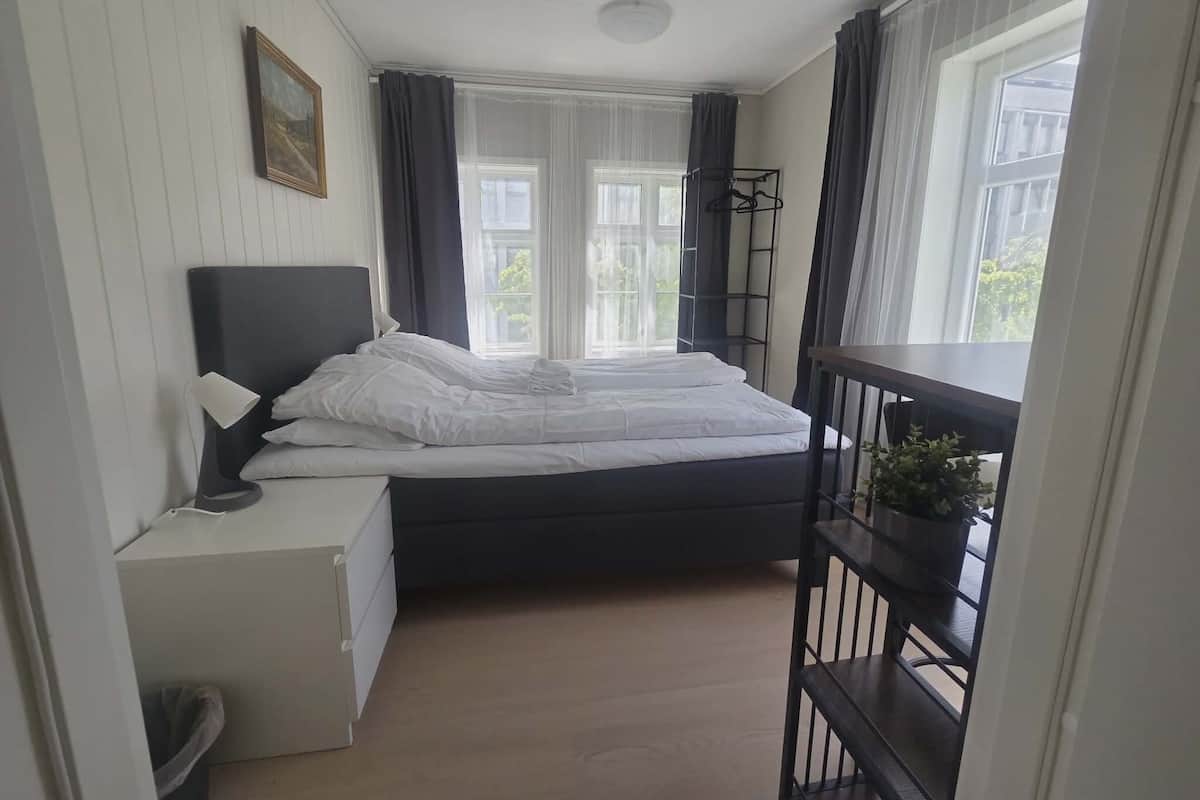 A bedroom with a bed, bedside table, lamp, and a window with curtains.