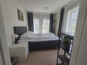 A bedroom with a bed, bedside table, lamp, and a window with curtains.