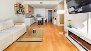 Ein modernes Wohnzimmer mit einer Couch, einem Glastisch, einem Kamin und einer Küche im Hintergrund.