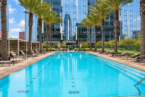 A swimming pool with lounge chairs and palm trees, surrounded by a modern building with reflective glass windows. - Resort Living - Olympic Amenities, 24/7 Security, Free Parking, Gym, Sauna (Los Angeles)