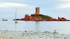 Eine felsige Insel mit einem Turm, Booten im Wasser und einem Kiesstrand.