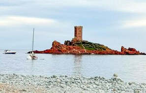 Eine felsige Insel mit einem Turm, Booten im Wasser und einem Kiesstrand.