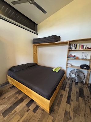 A room with a wooden bed, a ceiling fan, a bookshelf, and a fan on the floor.