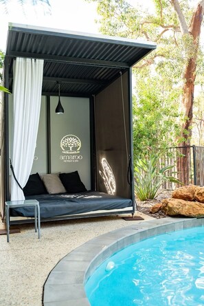 A modern outdoor lounge area with a pool, a bed with pillows, and a logo for 'amargo RETREAT & SPA'.