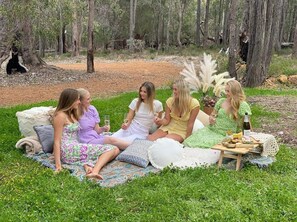 A group of people sitting on a blanket in a grassy area with trees in the background.