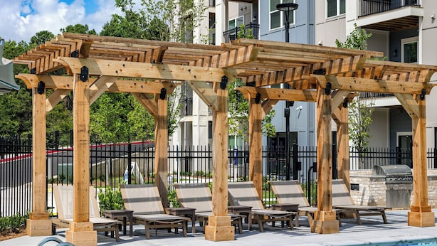 Une pergola en bois avec des fauteuils et une piscine.