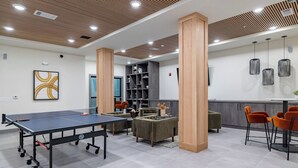 Une table de ping-pong, des canapés, une bibliothèque et des suspensions lumineuses dans un espace intérieur moderne.