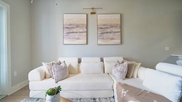 A living room with a white sofa, a coffee table, and two wall-mounted paintings.