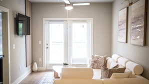 Un salon comprenant un canapé, une table basse, un téléviseur fixé au mur et un ventilateur de plafond.