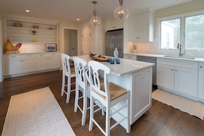 A modern kitchen with white cabinetry, a central island with bar stools, a stainless steel refrigerator, and pendant lighting.