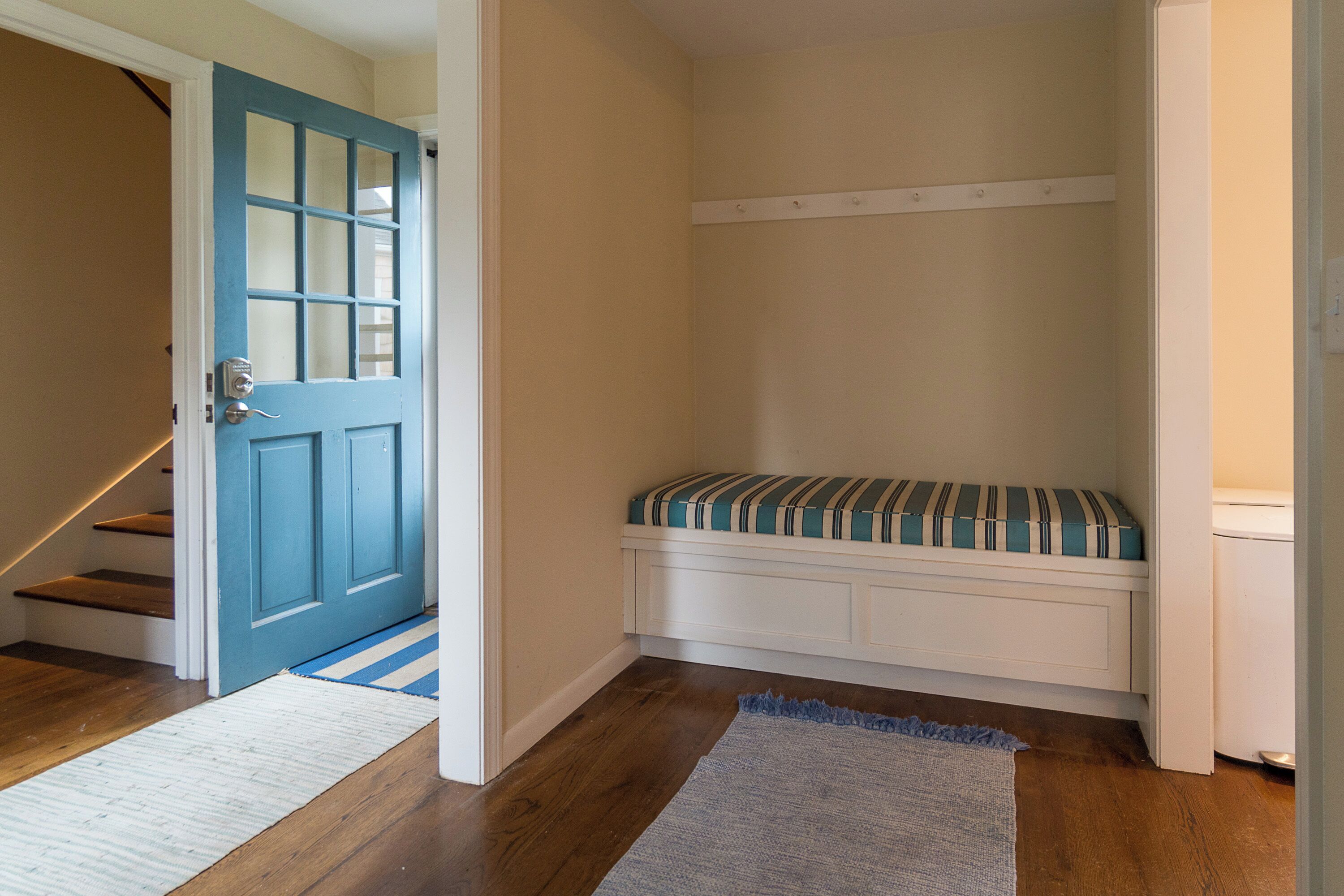 A room with a blue door, a bench with striped cushions, a white bench, and a wooden floor.