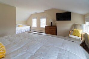 A bedroom with a large bed, a dresser, a chair, and a television on the wall.