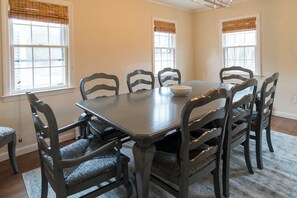 A dining room with a rectangular table, six chairs, and two windows with blinds.