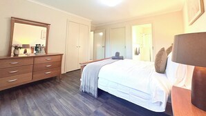 Una habitación de hotel con cama, cómoda, espejo, puerta y rejilla en el techo.
