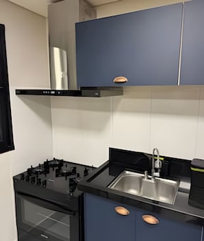 A modern kitchen with a black stove, stainless steel sink, and blue cabinets.