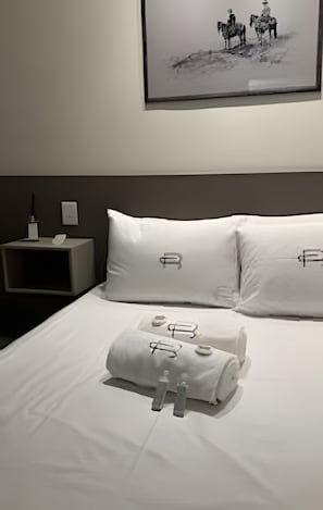 Habitación de hotel con una cama bien hecha, una mesita de noche con lámpara y un cuadro en la pared.