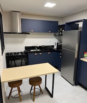 Una cocina compacta con una mesa de comedor, dos taburetes, un refrigerador y una estufa.