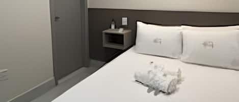 Una habitación de hotel con una cama, una mesita de noche, un cuadro enmarcado en la pared y una puerta.
