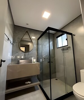 A modern bathroom with a glass-enclosed shower, a white toilet, and a vanity with a mirror.